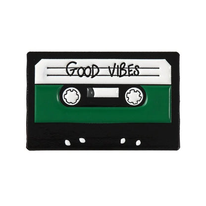 Valga's Punk Music Lovers Enamel Pin is designed to resemble a vintage audio cassette tape, perfect for punk music enthusiasts. The pin features a black, white, and green color scheme with the words "Good Vibes" written on the label section.