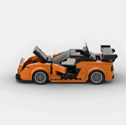 A LEGO model of an orange sports car with opening doors, trunk, and hood. Inspired by the iconic Mazda design, this Valga Lego Car Mazda features a sleek build with detailed elements like black-tinted windows and a rear spoiler. The grey wheels add contrast to the vibrant orange body against a plain white background.