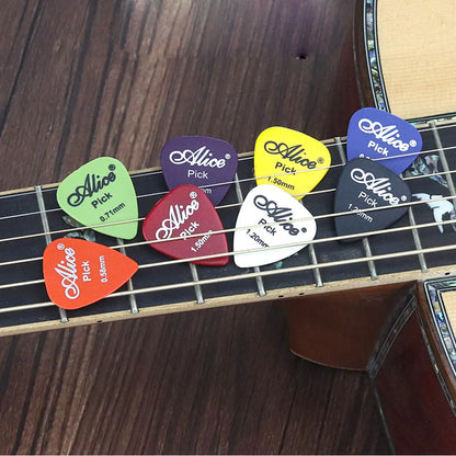 Several colorful, durable guitar picks are placed on the fretboard of an acoustic guitar. These Valga-branded ABS plastic picks vary in thickness from 0.71mm to 2.50mm and come in colors such as green, red, purple, black, white, yellow, and blue.