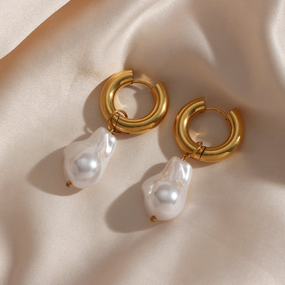 A pair of Valga's Water Drop Earrings, featuring gold hoop earrings with irregularly shaped baroque pearl charms, are displayed on a soft, beige satin fabric. The stainless steel hoops showcase a polished, shiny finish while the pearls hang delicately from the hoops.