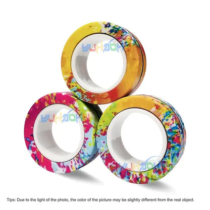 Three Valga 3Pcs Magnetic Rings Anti-Stress are stacked in a pyramid. Each ring showcases a colorful design with splashes of vibrant colors including yellow, pink, blue, and green against a plain white background. Much like fidget spinners, these rings bring an element of fun to your projects. A printed text at the bottom notes potential color variations due to lighting.