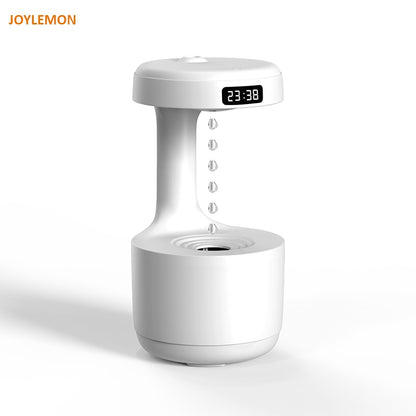 White desk fountain featuring a sleek, modern design and an LED clock display showing "23:38." Water droplets are suspended mid-air as if falling into the basin below. The device boasts Valga's whisper-quiet technology. The brand name appears in the top left corner.