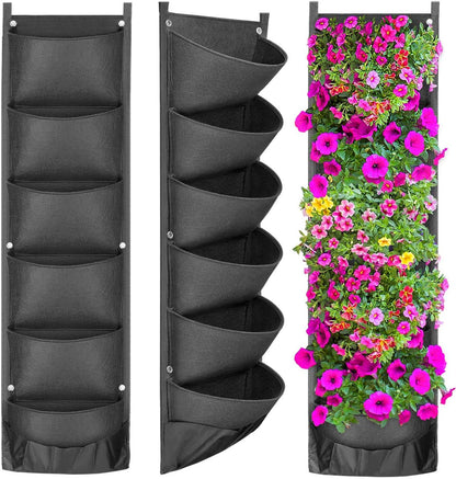 Three **Valga Vertical Hanging Garden Flower Pots** are displayed. The left and middle planters, made from environmental protection felt cloth with six pockets each, are empty and black. The right planter is filled with vibrant pink and purple flowers. These pocket garden systems have grommets at the top for easy hanging.