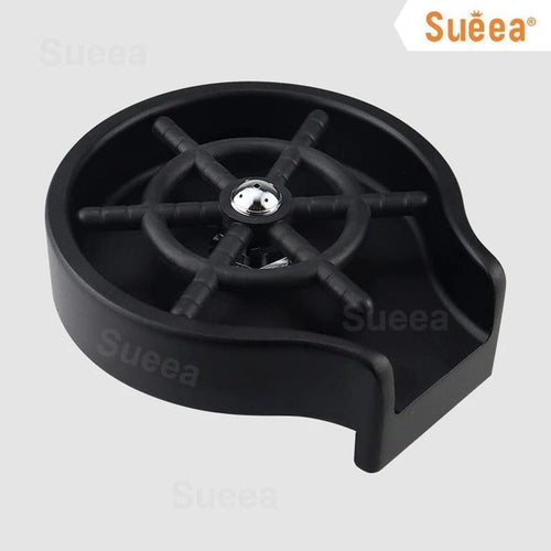 A black countertop Valga "Glass Rinser Automatic Cup Washer" is shown against a white background. The Glass Rinser features a circular base with high-pressure water jets arranged in a star pattern and an open-sided design for easy placement and removal of glasses.