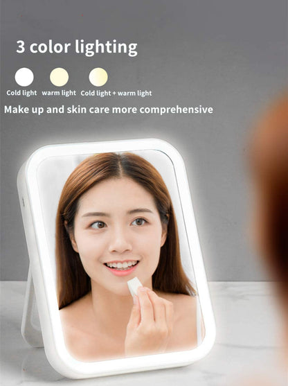 A woman is looking into the Valga Smart Makeup Mirror, a rectangular lighted mirror offering three lighting options: white, yellow, and mixed. She holds a makeup sponge near her face. Text on the image reads, "3 color lighting - cold light, warm light, cold light + warm light." Make your makeup and skin care routines more comprehensive with this innovative mirror from Valga.