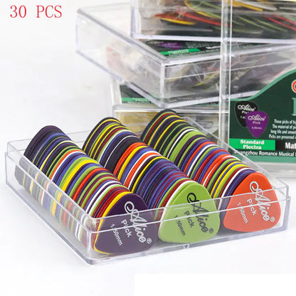 A clear plastic container from Valga holds multiple colorful, durable guitar picks arranged neatly in rows. Each ABS plastic pick has "Valga Pick" and different size notations printed on it. In the background, another similar container with more acoustic electric bass picks is partially visible. "30 PCS" is written in red text.