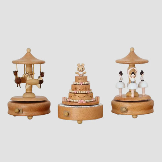 Three **Valga Vintage Wood Music Boxes** are displayed against a plain background. The first features a carousel with animals, the second showcases a tiered cake with a teddy bear topper, and the third depicts two ballerinas in dance poses. These nostalgic decor pieces make for perfect heirloom gifts.