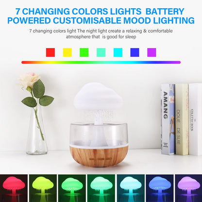 An image of the Valga Desktop Rain Cloud Humidifier, featuring 7 changing colors including red, yellow, green, cyan, blue, purple, and white. The humidifier doubles as an aromatherapy diffuser to create a soothing atmosphere. It is placed on a wooden base next to several books and a vase with a green plant. Text at the top describes the humidifier.