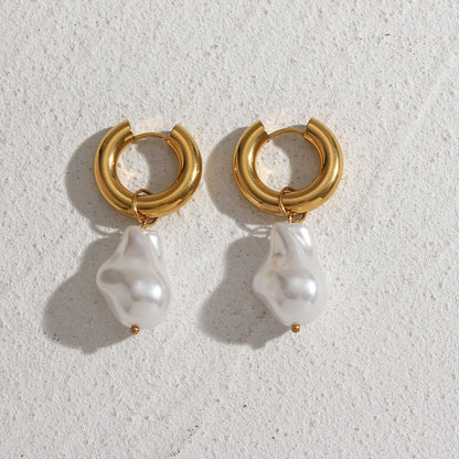 A pair of gold hoop Water Drop Earrings by Valga with white baroque pearl pendants displayed on a textured, light-colored surface. The pearls are irregularly shaped, adding a unique and organic look to the elegant design of these baroque pearl charm earrings.