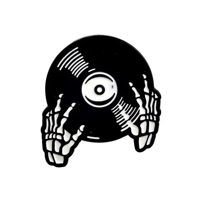 Introducing the Punk Music Lovers Enamel Pin by Valga: An illustration of white skeletal hands clutching a black vinyl record, designed especially for punk music enthusiasts. The record features white highlights that represent reflections or grooves, with a central white label. Set against a plain backdrop, this pin captures the rebellious essence of the punk movement perfectly.