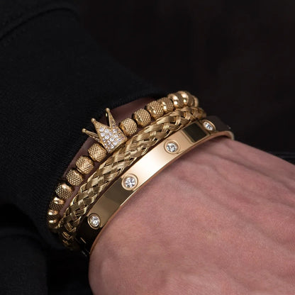 A close-up shot of a wrist adorned with multiple luxury Valga Diamond Roman Bracelets. The collection varies in design, featuring a beaded bracelet with a crown charm, a woven bracelet, and a sleek band embedded with gems - showcasing exceptional craftsmanship. The person is wearing a dark long-sleeve shirt.