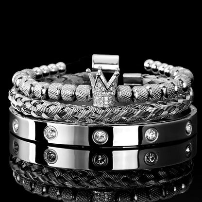 The Valga Diamond Roman Bracelets set is elegantly displayed on a black reflective surface. This luxurious collection includes four bracelets—featuring beaded, braided, and solid metal bands. One standout piece crafted from stainless steel showcases a crown-shaped ornament adorned with small gemstones, while another bracelet is embedded with clear crystals, exemplifying exceptional design.