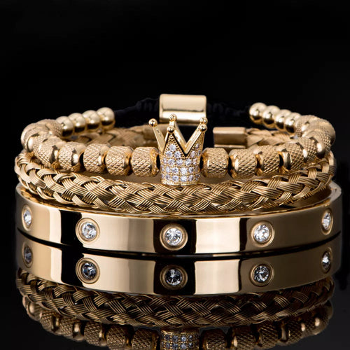 A stack of Valga's luxurious Diamond Roman Bracelets, crafted from gold and stainless steel with varying textures and designs, rests on a reflective black surface. Some bracelets feature braided patterns and round beads, while others are smooth with embedded gemstones. Standing out in the collection is an exceptional design with a crown-shaped charm adorned with gems.